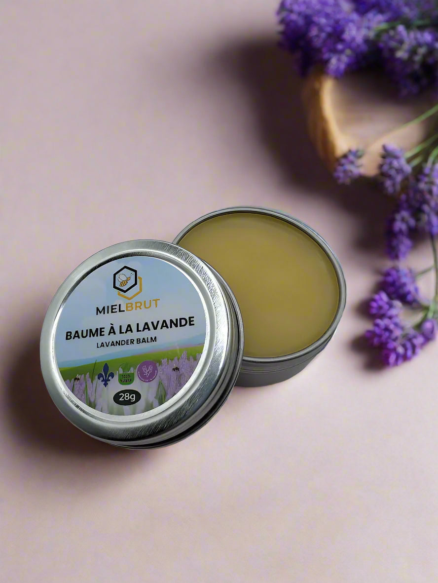 A tin of "Lavender Beeswax Balm 1oz" from Mielbrut.com sits on a textured surface, revealing a creamy balm perfect for dry skin. Its label, featuring lavender illustrations, emphasizes natural ingredients and weighs 28g.