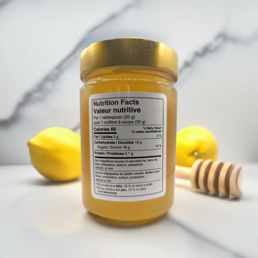 A jar of Beekeeper's Special Reserve: Exceptional Catalpa Honey from Mielbrut.com with its nutrition facts label displayed, placed on a white surface. In the background, two whole lemons and a wooden honey dipper coated with honey add a fresh and natural vibe to the scene. The focus is on the label, highlighting this limited edition product born from beekeeping passion.