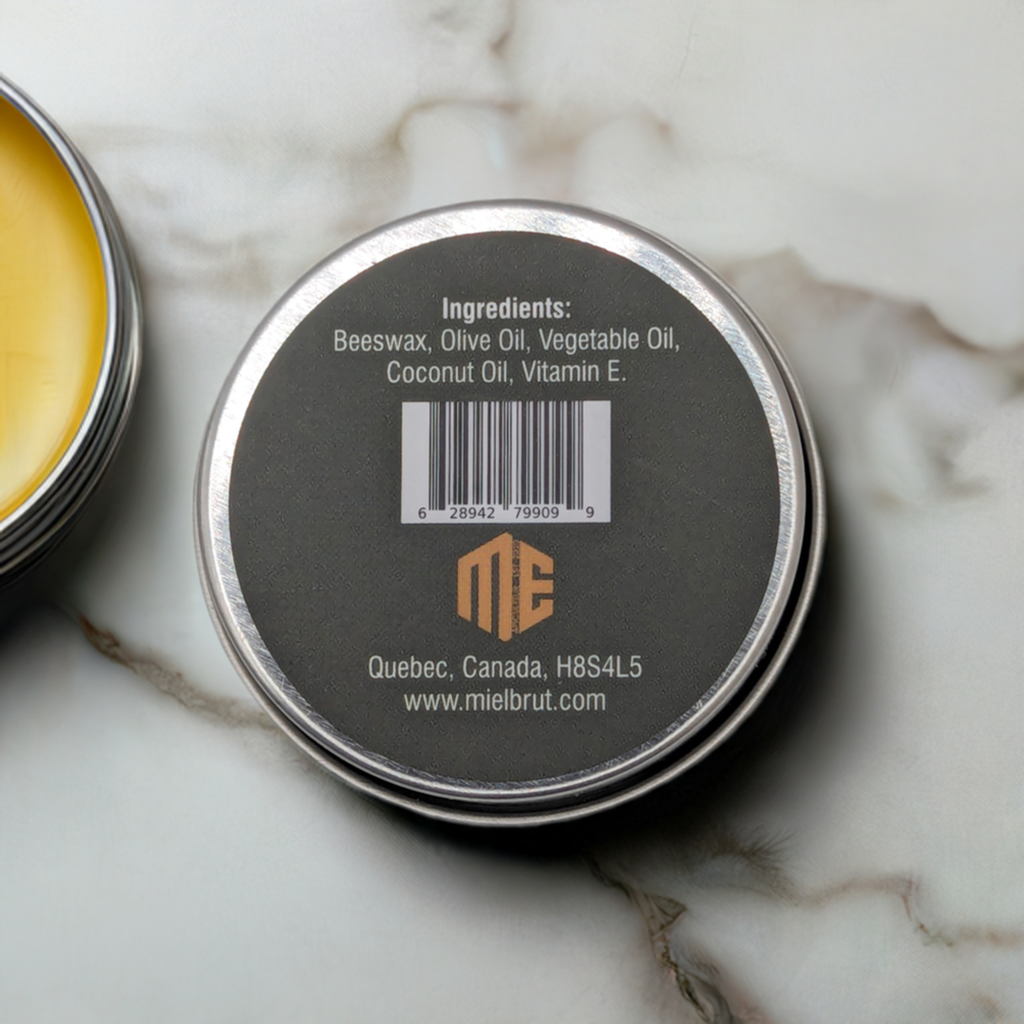 A small metal tin with a dark gray lid is shown. The label on the lid reads "Ingredients: Beeswax, Olive Oil, Vegetable Oil, Coconut Oil, Vitamin E." This honey-infused balm also displays a barcode, the Mielbrut.com logo, and an address: "Quebec, Canada, H8S4L5." The product name is "Beeswax Balm: Moisturizer for lips, hands, feet and skin.