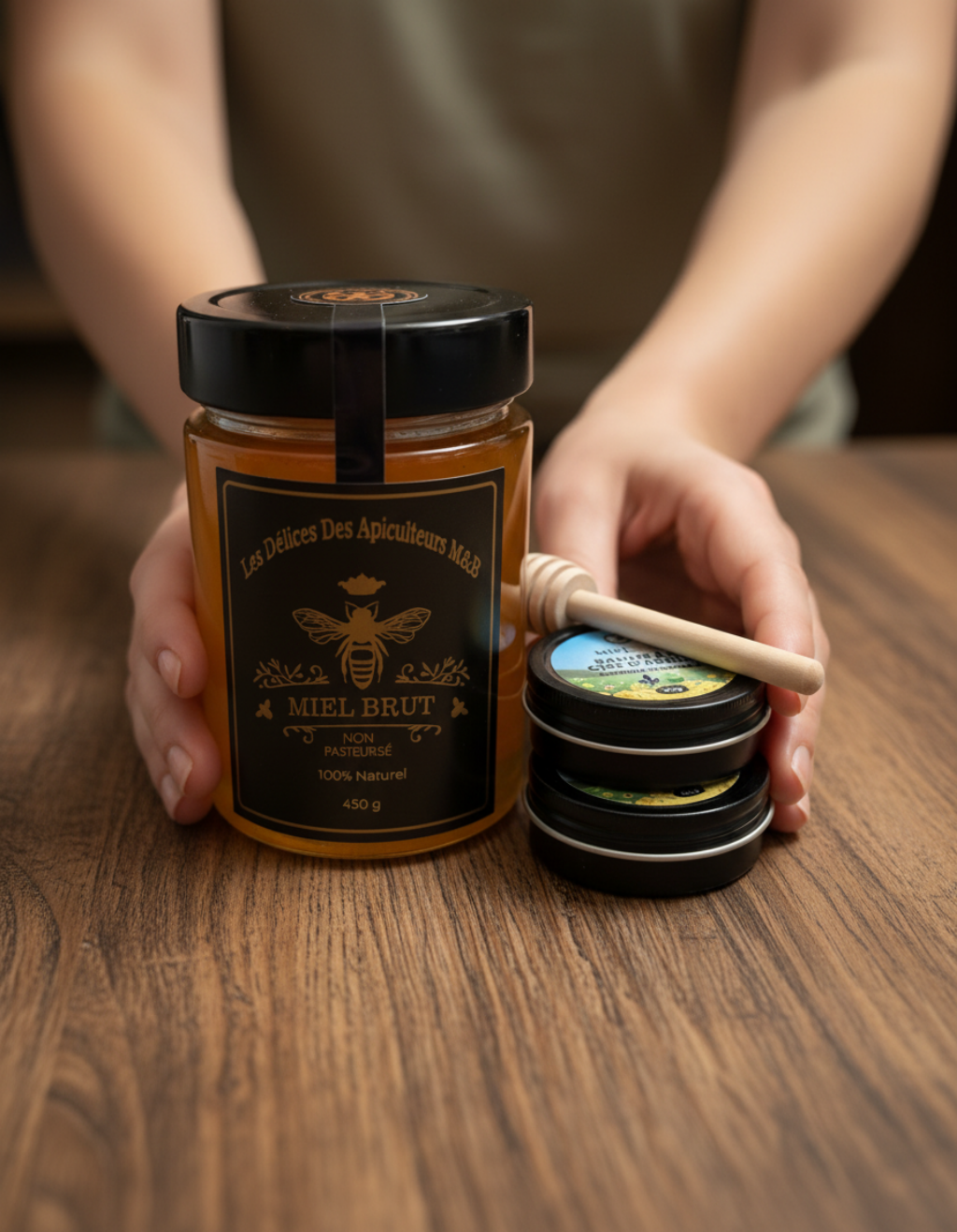 A person holds a jar of Mielbrut.com honey and a dipper, with two black-lidded tins from the Build‑Your‑Own Honey & Balm Gift Set displayed on a wooden table.