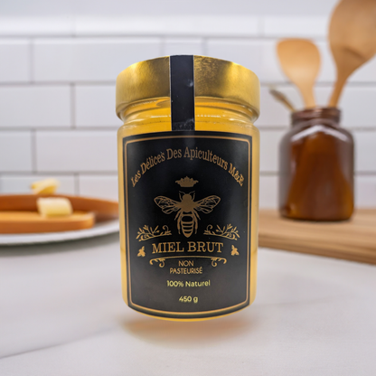 A jar labeled "Beekeeper's Special Reserve: Exceptional Catalpa Honey" from Mielbrut.com sits on a kitchen counter. The label, showcasing a bee logo, proudly declares "Non Pasteurisé" and "100% Naturel". Brimming with beekeeping passion, this Special Reserve Honey exudes authenticity. In the background, kitchen utensils and another jar are visible.