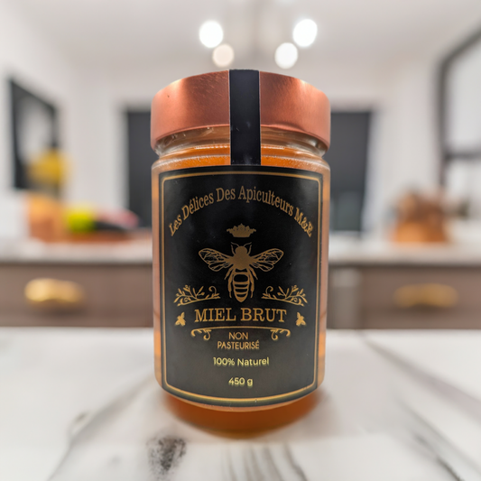 A jar of "Beekeeper's Amber Wildflower Honey" by Mielbrut.com with a black and gold label sits on a kitchen counter. The label reads "100% Natural," "450g," and the background is blurred.