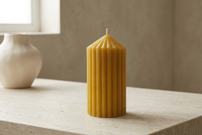 Ribbed beeswax pillar candle beside a ceramic vase