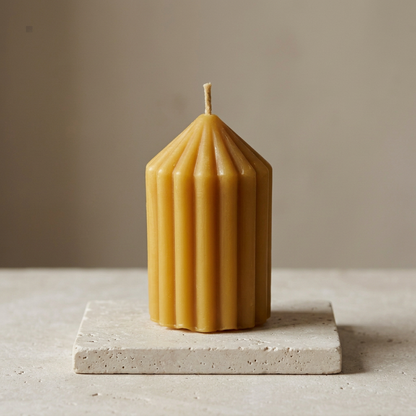 Elevated view of the Stubby beeswax candle showing its pointed top and deep ribs on a limestone slab.