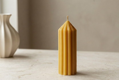 Golden ribbed beeswax pillar candle beside a cream vase