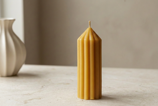 Golden ribbed beeswax pillar candle beside a cream vase